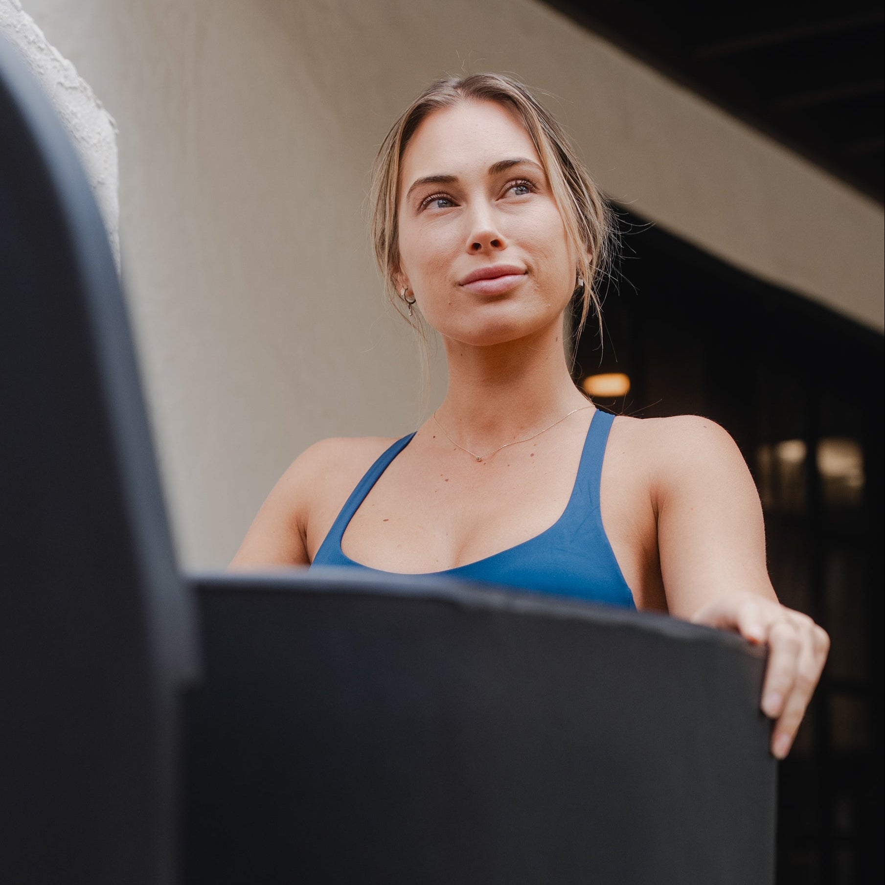 Woman in a blue sports bra top standing in a black cold plunge tub looking off into the distance