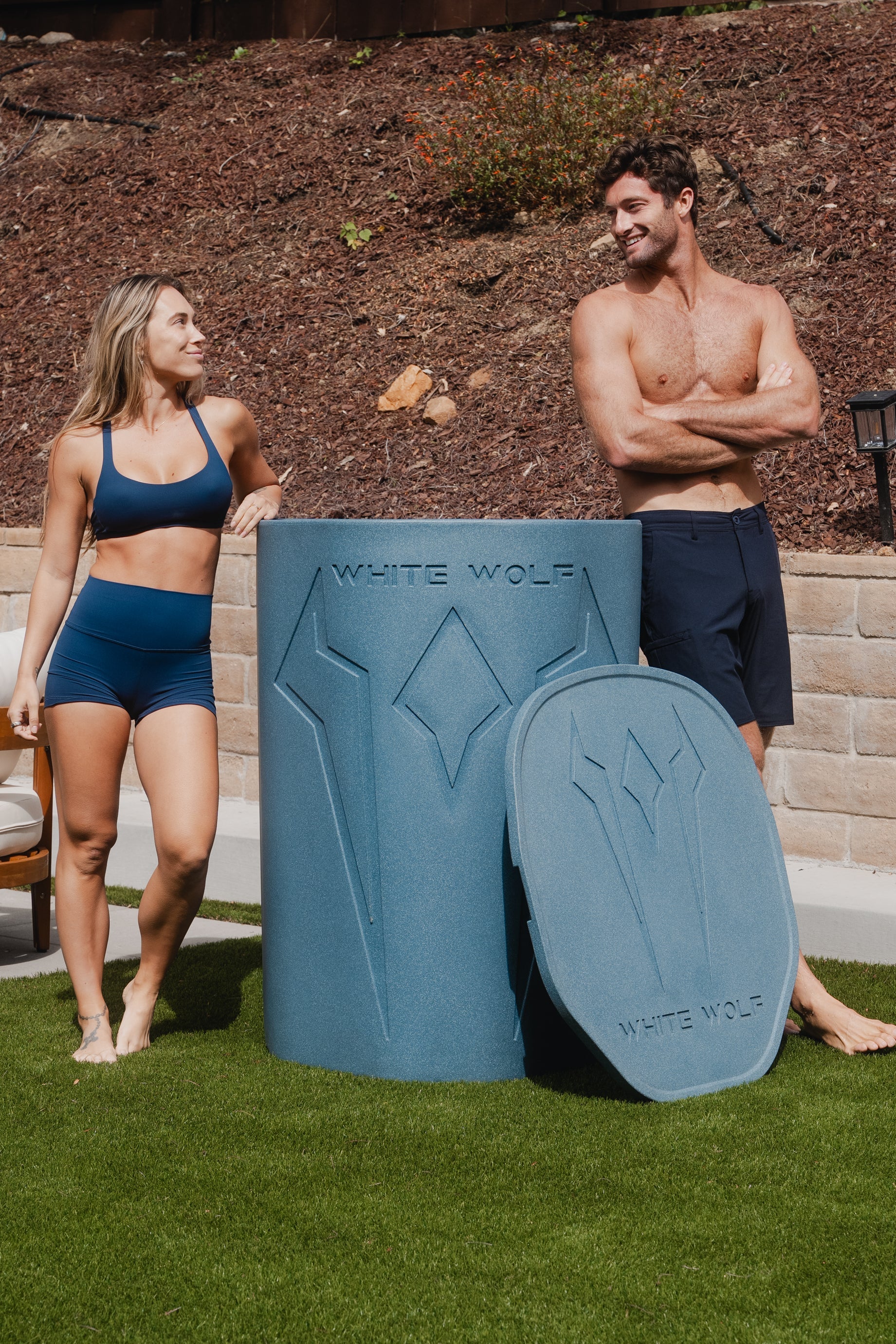 Two people standing next to a blue cold plunge container with 'White Wolf' branding in an outdoor setting.