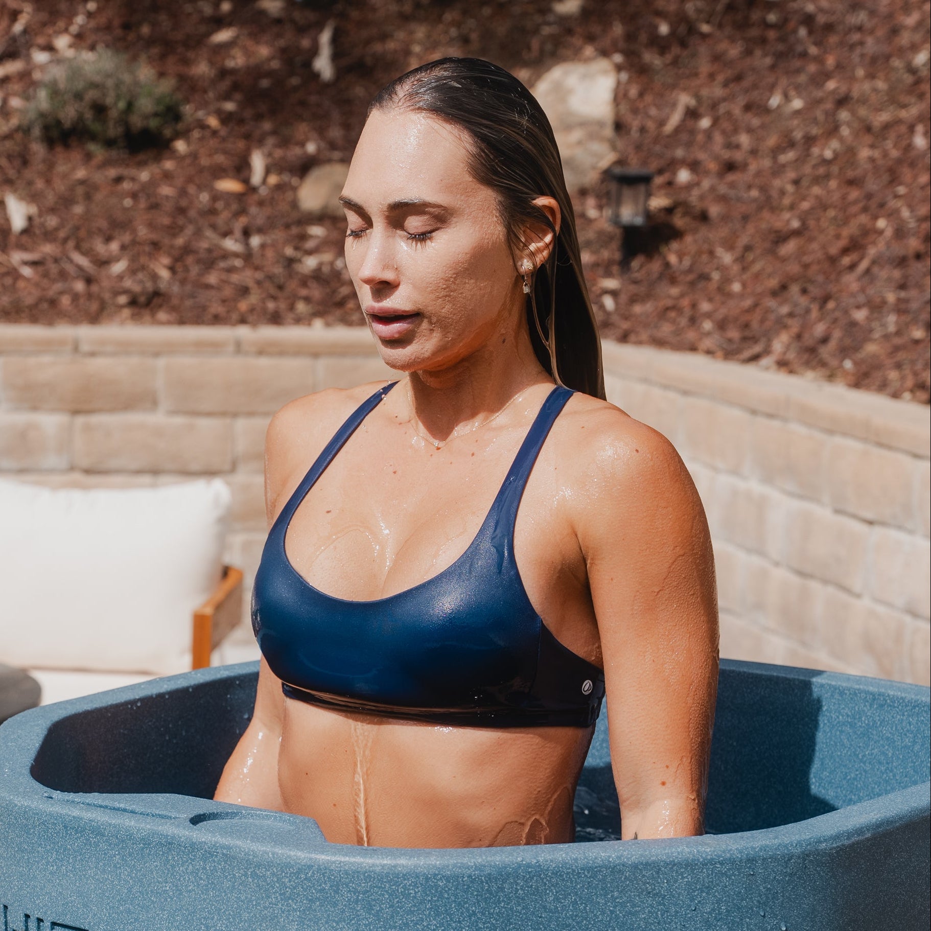Woman in a blue sports bra and shorts standing in a large blue cold plunge labeled 'White Wolf' outdoors.