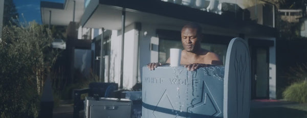 Man submerging in blue cold plunge while water flows over tub